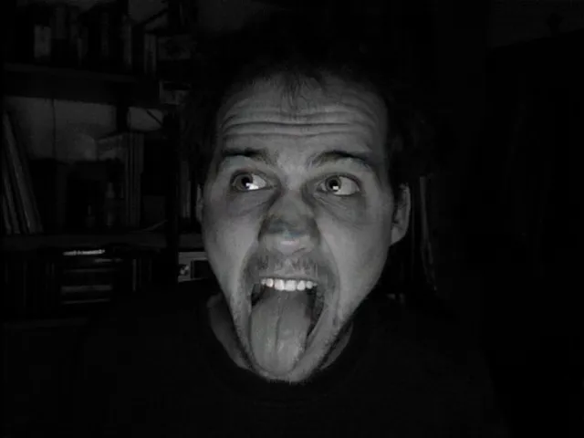 2007 — Portrait mit herausgestreckter Zunge in der Dunkelheit